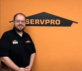 Male employee standing in front of SERVPRO wall, black polo 